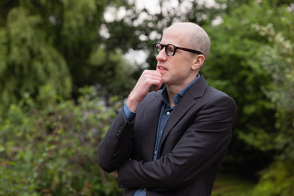 Outdoors portrait of Nick Bostrom looking to the left against a forest backdrop
